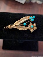 Front view of gold-tone floral brooch showing gold leaves and flower petals with turquoise cabochon stones.