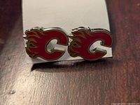 Front view of the pair of silver tone Calgary Flames cufflinks showing the logo in red and yellow enamel.