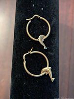 Pair of 10K gold hoop earrings with dolphin charms displayed on black background, showing full front view, hoops with dolphin pendants attached.