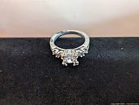 Front view of silver engagement style ring showing center stone and four side stones.