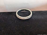 Silver eternity ring lying flat on black cloth, showing band with stones all around.