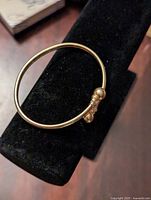 Photo of gold tone cuff bracelet displayed on a black velvet stand showing entire bracelet shape and design.