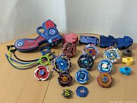 Photo showing multiple Beyblade tops and launchers arranged on a surface with visible metal parts and colorful designs.