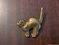 Front view of a metal cat brooch pin showing the detailed textured fur and raised tail.