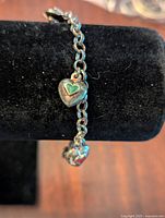 Close-up of the sterling silver chain bracelet with a green enamel heart charm attached to the chain.