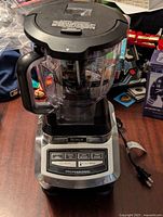 Front view of Ninja Professional blender showing clear plastic container with black handle and lid, stainless steel base with control panel and power cord.