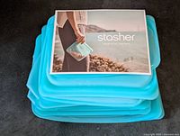Stack of six blue reusable silicone food bags with brand pamphlet on top