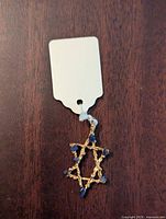 Photo of the gold-tone Star of David pendant with blue stone accents on a wooden surface, showing texture and stone details.
