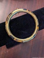 Top view of closed tiger's eye and gold tone metal bangle bracelet on black display stand.