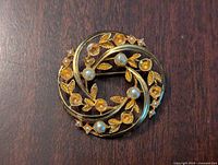 Front view of the circular vintage Art Nouveau brooch showing gold leaves, stems, embedded small pearls and amber-colored stones.