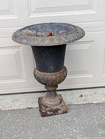 Front view of vintage cast iron urn planter showing scalloped rim and pedestal base with rust and weathering.