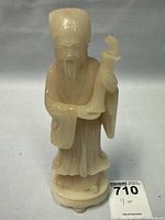 Front view of the carved alabaster or pale stone figurine of an elderly scholar holding a scroll, standing on a rounded base.