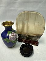 Full view of the blue cloisonné vase, translucent stone table screen on wooden stand, and carved wooden stand on white cloth background.