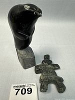 Photo of black soapstone seal and dark green soapstone Inukshuk with lot identification tag.