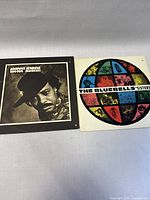 Front covers of vinyl albums: Johnny Jenkins 'Ton-Ton Macoute!' black and white portrait cover, The Bluebells 'Sisters' colorful circular design cover.