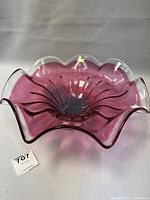 Top-down and angled views of a cranberry-colored art glass bowl with a clear ruffled edge and flowing curves, showing its size and design details.