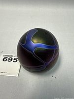 Spherical art glass paperweight with iridescent blue and purple design on the side view.