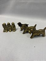Photo showing all four animal figurines: two brass Scottie dogs, one dark metal spaniel, and brass monkey trio on a plain white background.