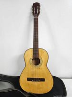 Front view of the vintage small classical guitar showing natural wood finish, rosette around sound hole, and white tuning pegs.