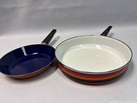 Two enamelware frying pans placed side by side, showing the interior surfaces and handles