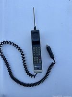 Front view of 1990s Motorola brick cell phone with antenna and coiled cord car adapter