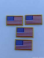 Photo showing four rectangular American flag patches with yellow border arranged in two rows on a white surface.