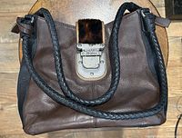 Full view of the brown leather purse showing braided black handles and front flap closure with buckle