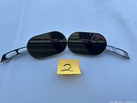 Pair of Harley-Davidson motorcycle mirrors with oval reflective surfaces and chrome stems with cut-out ovals, shown on white background.