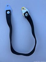 Black leather seat strap with metal triangular mounting plates at each end, shown laid out in a U shape on a white surface.