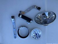 Five miscellaneous Harley-Davidson motorcycle parts displayed on a white background: chrome handlebar grip, two metal foot pedals, a chrome headlight reflector, and a chrome horn.