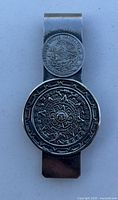 Close-up photo of a metal money clip with an Aztec calendar circular design on the bottom and a smaller circular Mexican eagle coin emblem on the top.