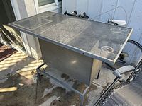 Outdoor metal mini bar table with a rectangular solid top surface, metal support frame and footrest bar.