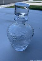 Clear glass round decanter with matching stopper placed on a flat surface outdoors in daylight, showing the full item from neck to base and stopper on top.