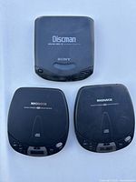 Top-down view of three portable CD players on a white background: one Sony Discman and two Magnavox units. No power cords are included.