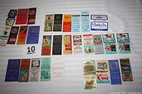 Top view of 30 vintage advertising match covers showing front designs with various colors, texts, and advertising logos.