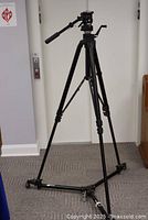 Full view of the black aluminum tripod mounted on the 3056 rolling base with adjustable legs and dolly wheels on carpet