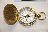 Top-down view of brass compass with lid open showing compass dial and needle.