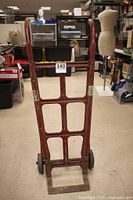Front view of the red vintage hand truck showing the metal frame grid structure and wooden handles with wheels at the bottom.