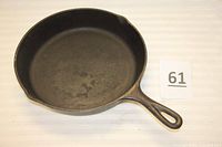 Top view of a cast-iron skillet showing cooking surface and two pour spouts, marked with lot number.