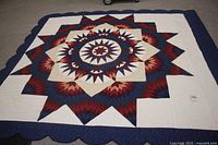 Full view of king size bedspread laid flat showing large colorful star pattern and dark blue scalloped edges on carpet floor.