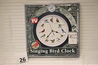 Original packaging box of the Singing Bird Clock, showing 25th Anniversary Edition branding, bird illustrations, and features of the clock.