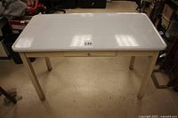 Front view of table showing white enamel ware top, beige legs and frame, with inventory label 146 on top.