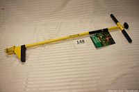 Full view of the yellow Hound Dog weed puller tool showing length, handles, and claw rooter at the bottom against a white background.