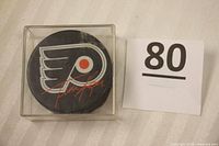 Top view of the puck inside the clear display case showing Philadelphia Flyers logo and Tim Kerr's signature in orange.