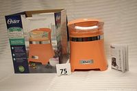 Oster ice cream maker in its original box, box shows product image and branding, user guide visible beside unit.