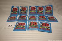 Set of thirteen Topps 3-D Baseball Stars cards in original unopened packets from 1985, arranged in rows on surface.