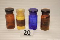 Four vintage apothecary jars lined up front view, showing colors and labels