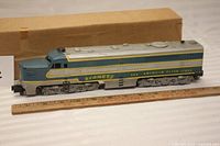 Side view of the blue and silver plastic diesel locomotive engine with yellow decals reading '466 Comet' and 'American Flyer Lines'. The locomotive is positioned beside a ruler showing its length around 13 inches, with a cardboard box in the background.