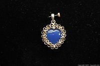 Front view of the heart-shaped pendant with a blue opaque stone set in detailed sterling silver filigree on a black background.