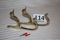 Two brass duck head wall hooks side by side showing overall shape and included mounting hardware screws and anchors.